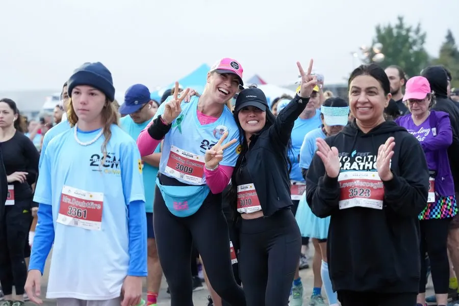 A group of runners, some smiling and posing with peace signs, at the start of a marathon.