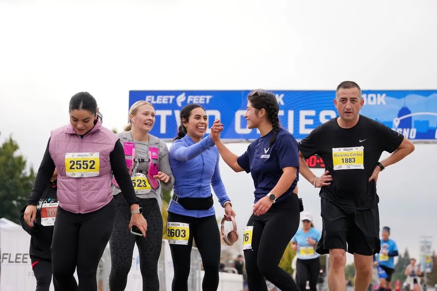 Runners smiling and high-fiving at the start of a race, with bib numbers visible.
