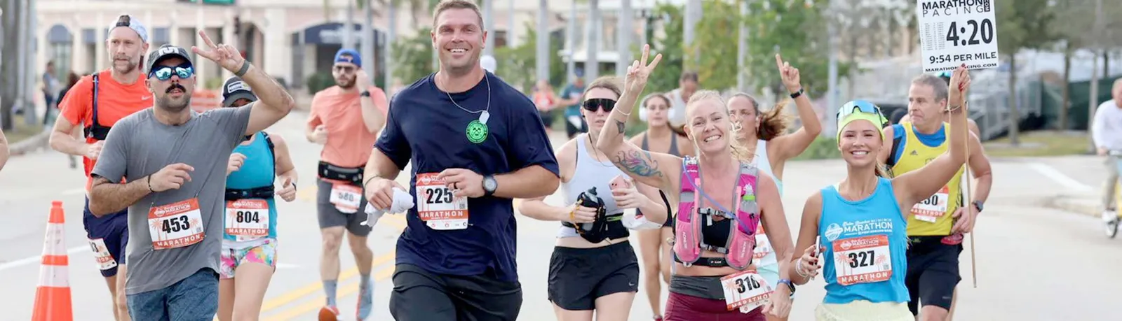 Runners smiling and waving as they participate in a marathon, with bib numbers visible.