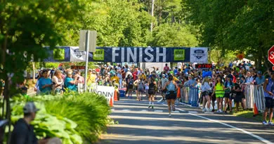 Runners crossing the finish line at the UConn Health Half Marathon, with a large crowd cheering them on under a "FINISH" banner.