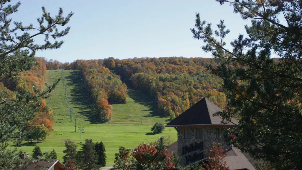 Scenic view of a mountain slope with autumn foliage and ski lifts, with a building in the foreground.