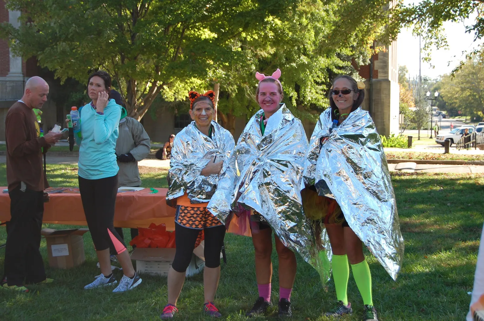 Three runners in Mylar blankets, two with face paint and costumes, smiling after a race.