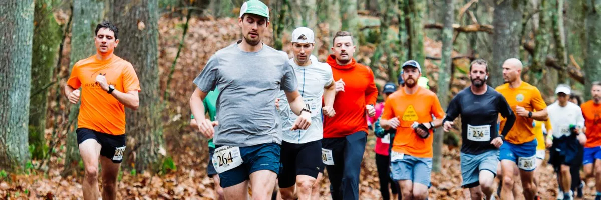 A group of male runners race through a forest on a trail course.
