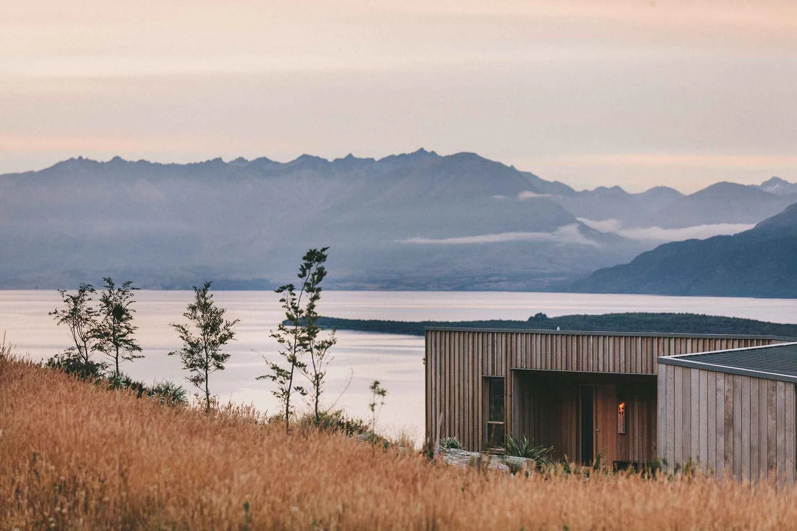Scenic view of a lake and mountains at dusk, with a modern building in the foreground.