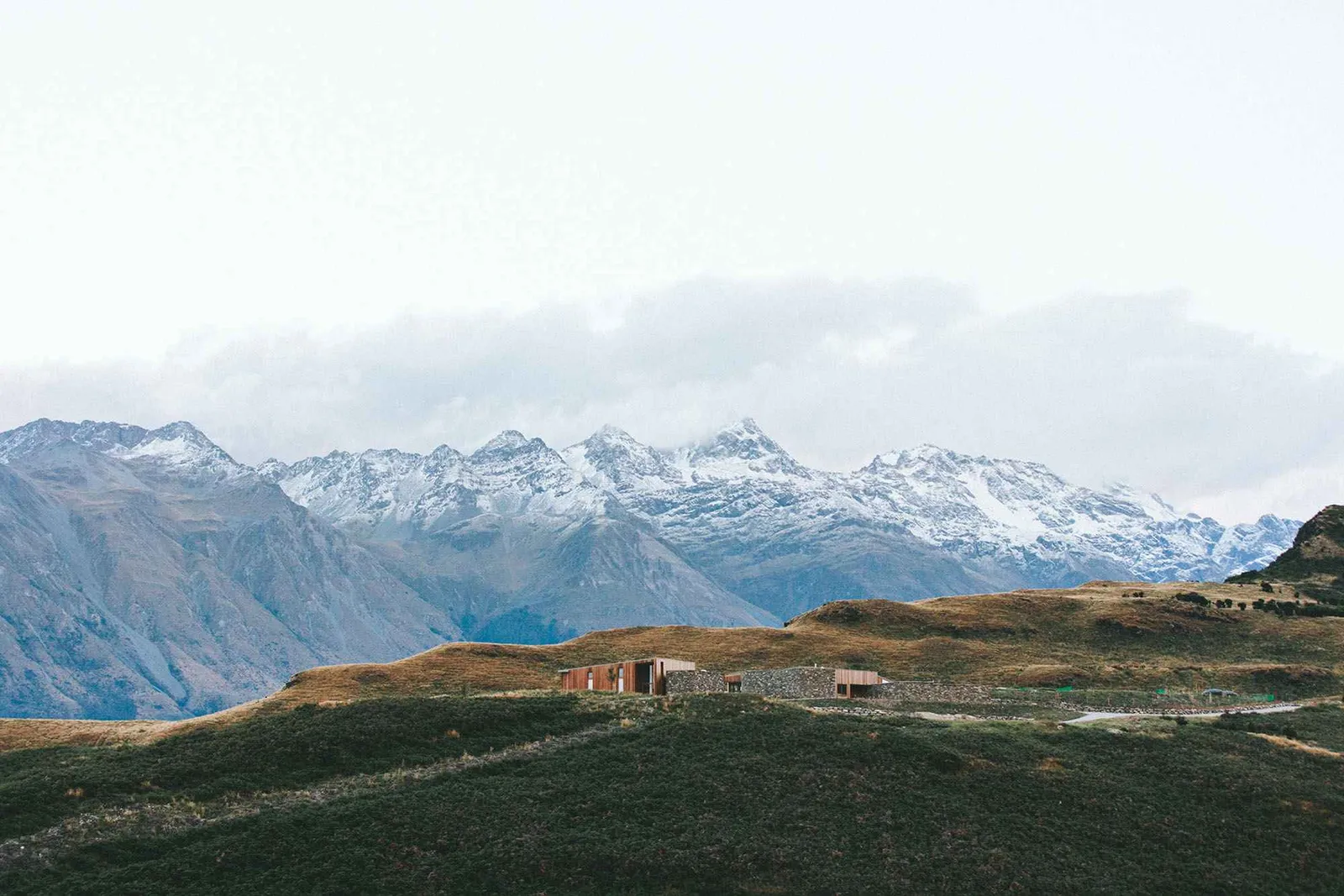 Scenic view of snow-capped mountains with a road winding through rolling hills.