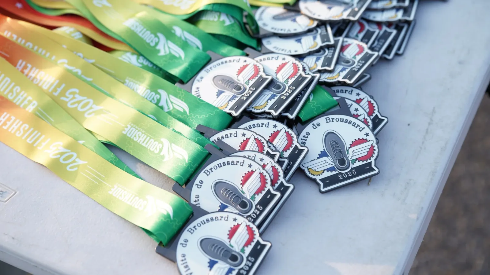 A pile of race medals and finisher ribbons for the 2025 Broussard race.