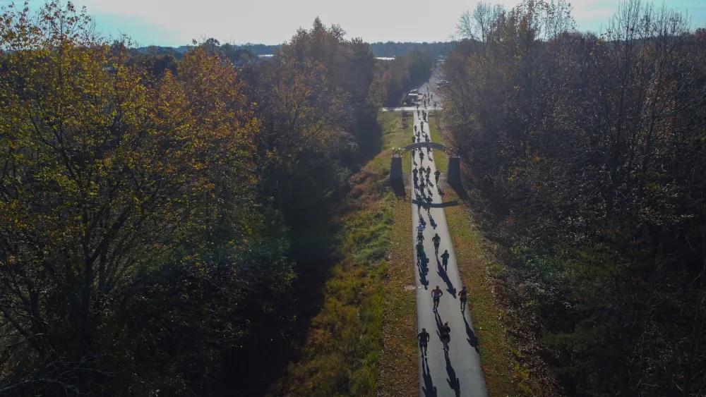 Runners on a paved path surrounded by trees with autumn foliage.