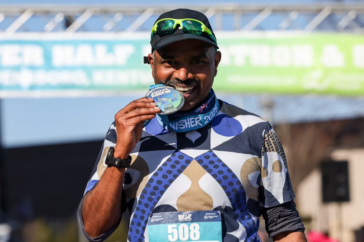 A smiling runner holds up their finisher medal after completing the Wendell Foster Half Marathon & 5K.