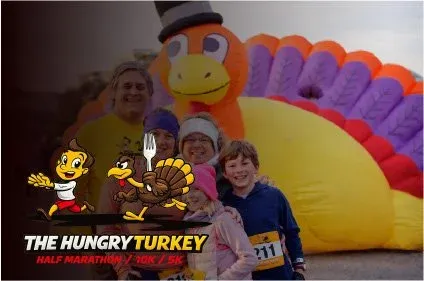 A group of people, including children, posing for a photo in front of a large inflatable turkey at The Hungry Turkey Half Marathon / 10K / 5K race.