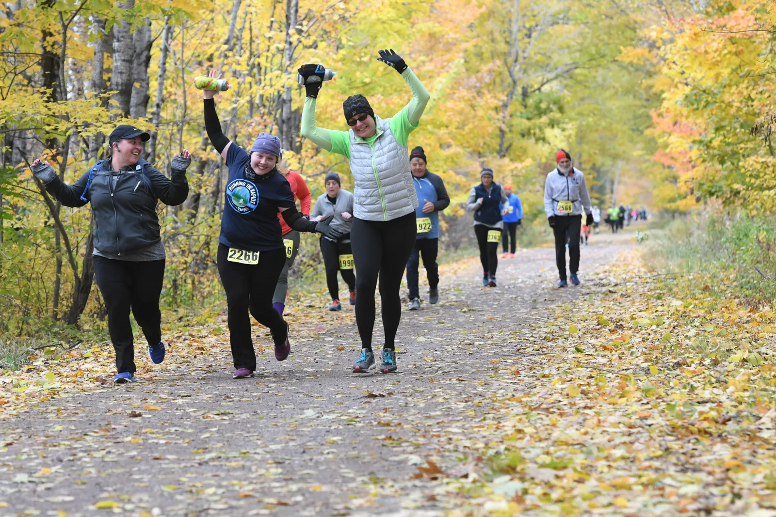 Runners celebrating on a path lined with autumn trees.