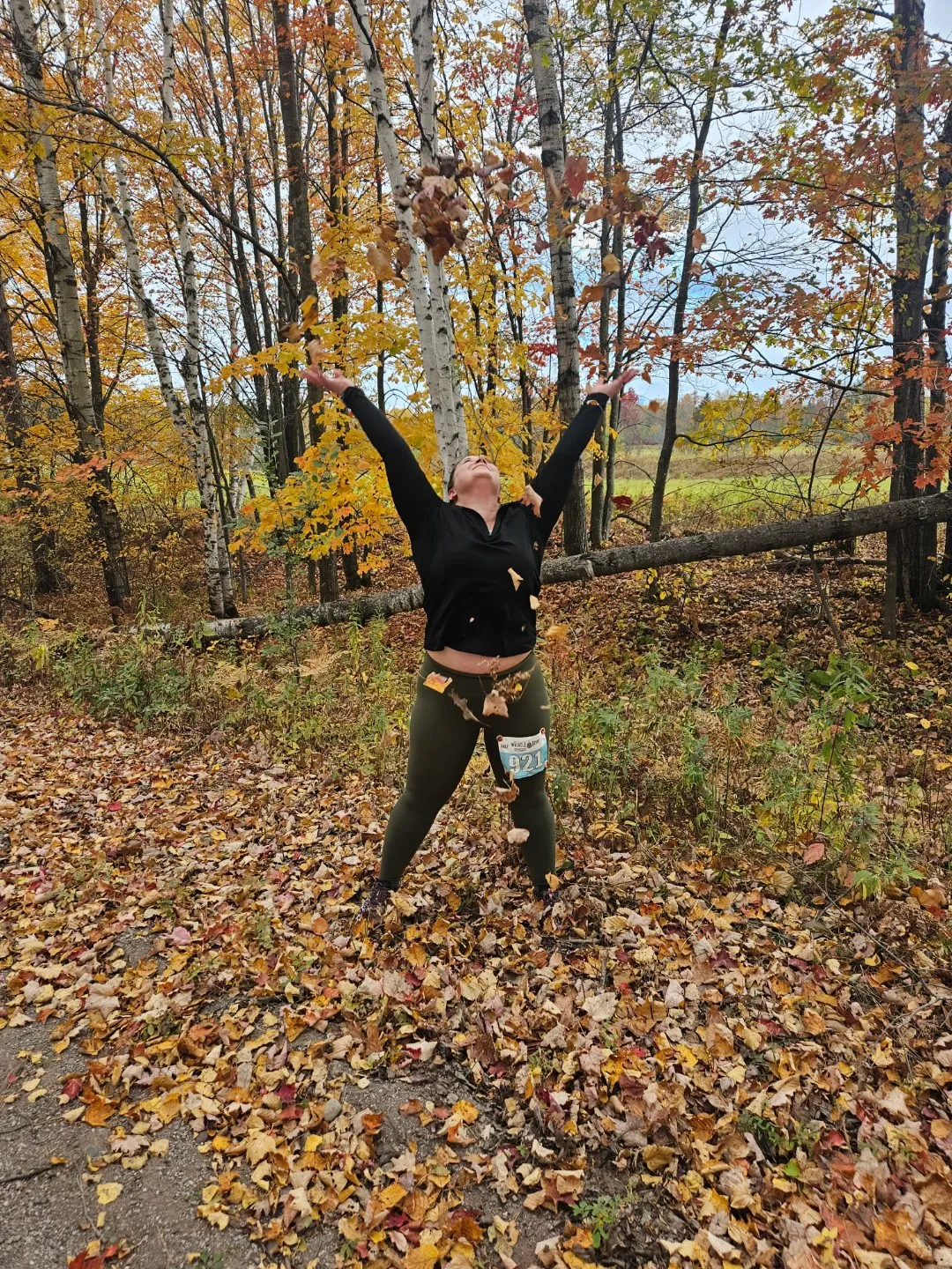 A runner throws leaves in the air on a wooded course during a fall race.
