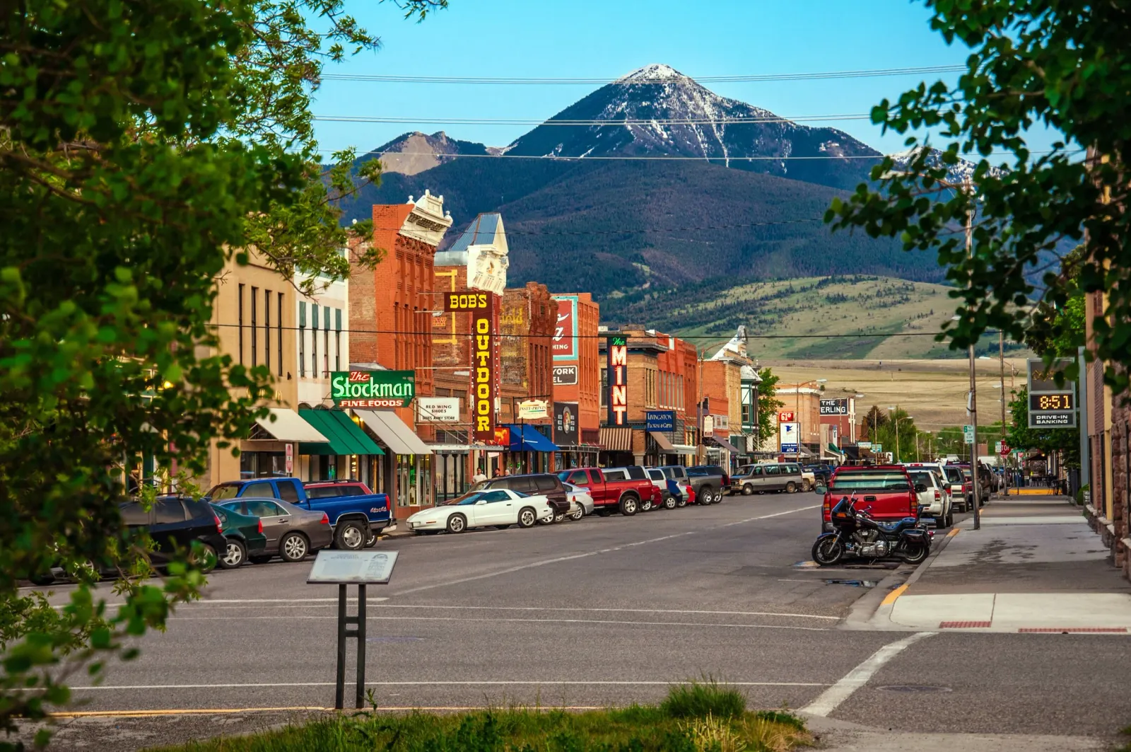 A street view of a small town with historic brick buildings and a large snow-capped mountain in the background.