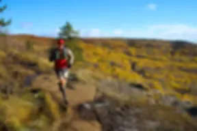 A runner on a trail with autumn foliage in the background.