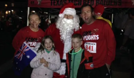 A family poses with Santa Claus at a race event, wearing race bibs and festive attire.