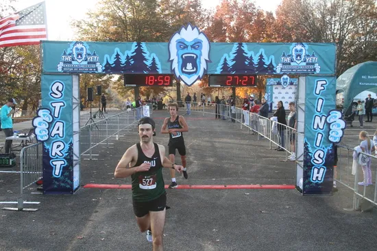 A runner wearing bib number 527 crosses the finish line under a large race arch with 'The Yeti' branding and digital timers.