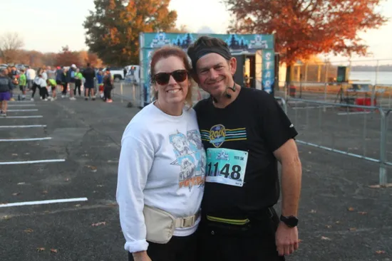 A smiling couple poses for a photo at the start line of a race, with other runners in the background.