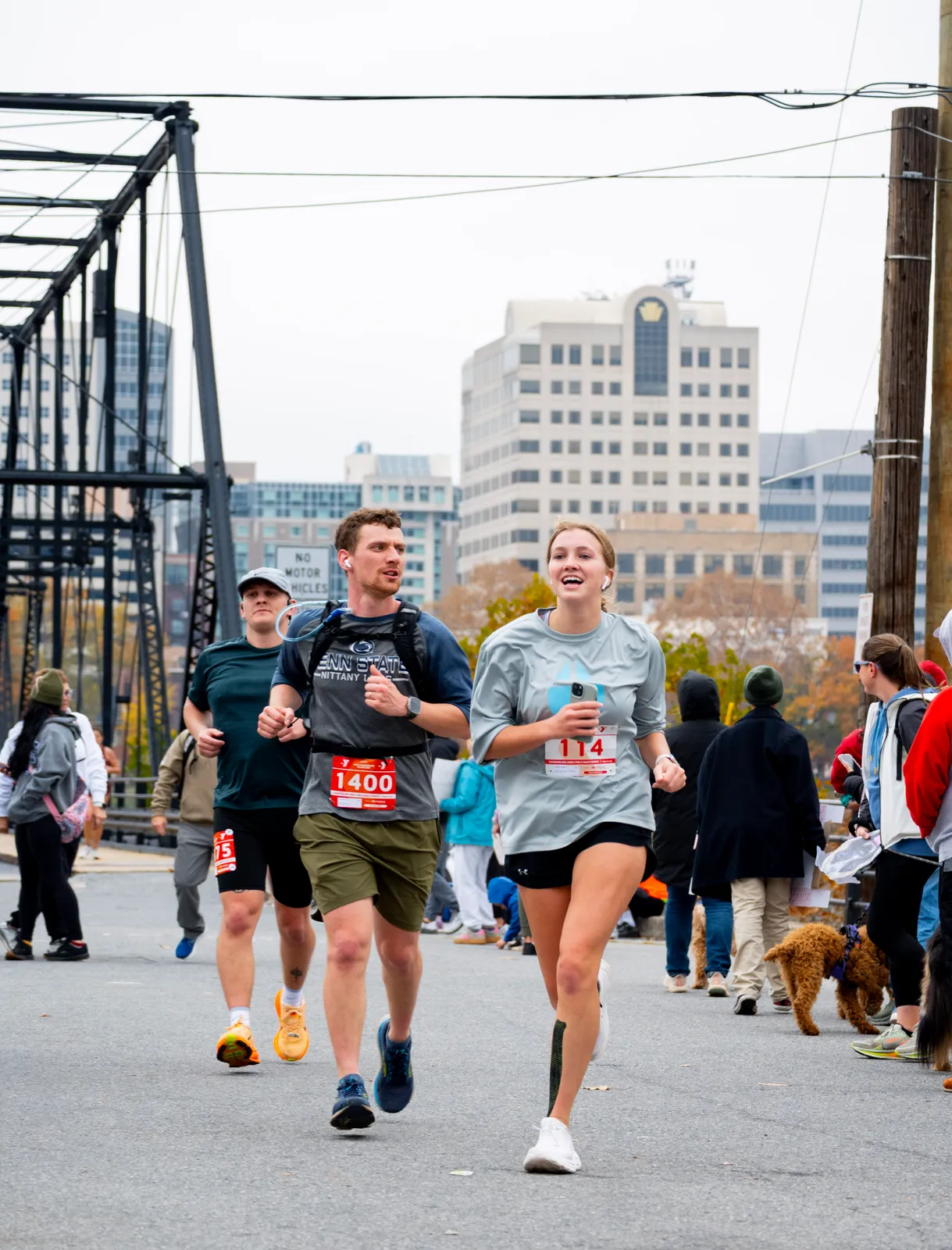Runners on a bridge during a race, with city buildings in the background.