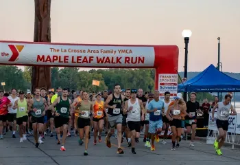 A large group of runners starting a race under a YMCA Maple Leaf Walk Run inflatable arch.