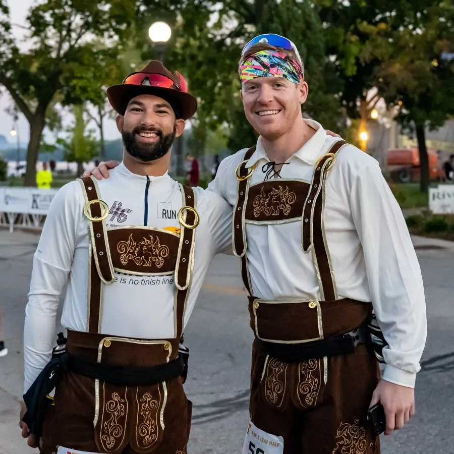 Two smiling male runners in traditional Bavarian-style outfits pose for a photo at a race event.