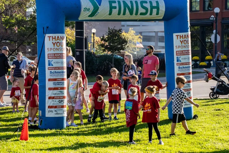 Children and adults gathered under a blue inflatable arch with 'The Finish' banner, some wearing race bibs.