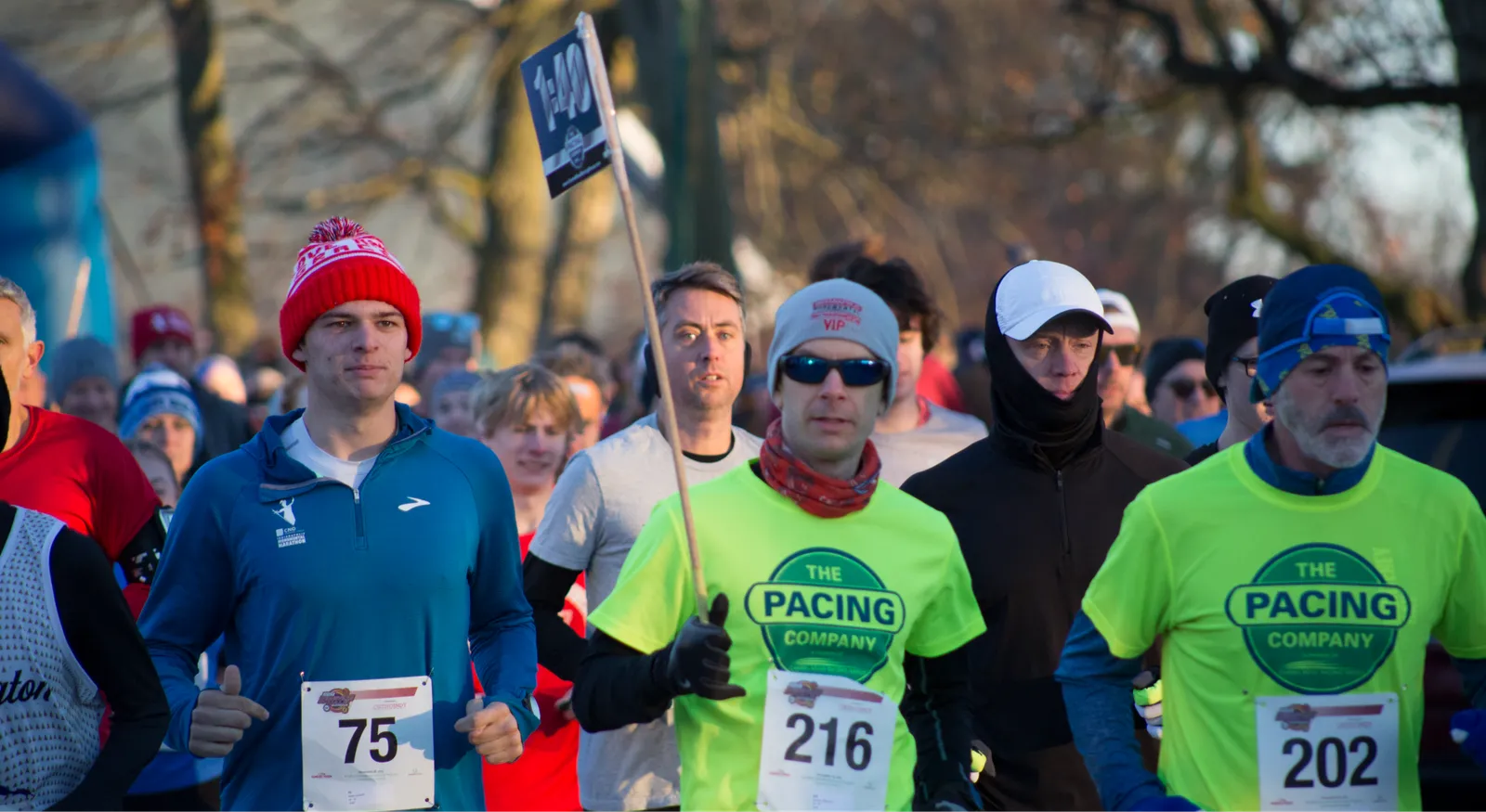 Runners in bright shirts and hats at the start of a race, with bib numbers visible.