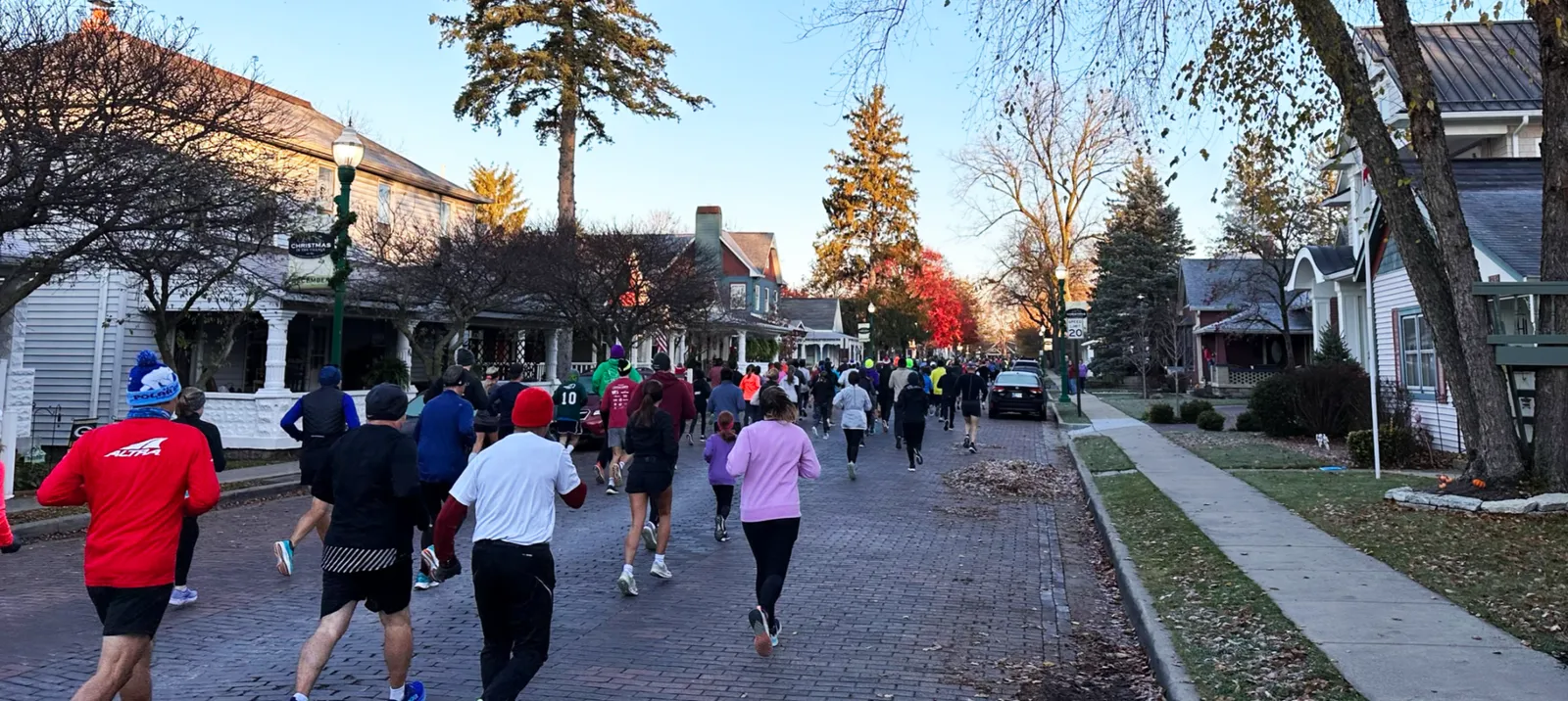 Runners participating in a race on a tree-lined street with houses on either side.
