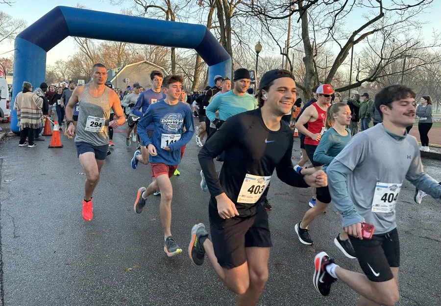 Runners starting a race under a blue archway, with many participants in the foreground and background.